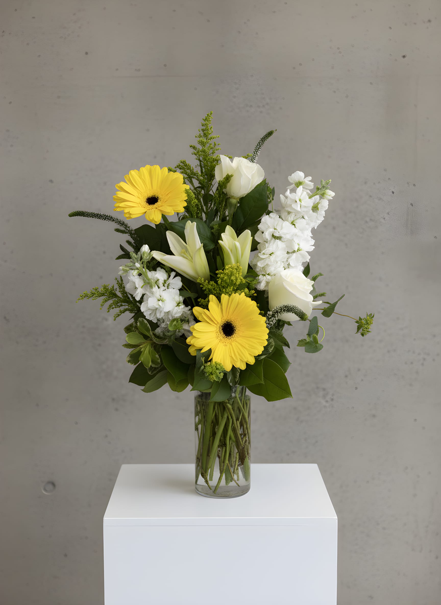 Yellow gerbera daisies and white lilies in a clear glass vase