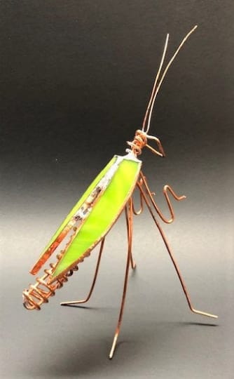 #A020 - Lime Green Praying Mantis - A bright lime-green stained glass praying mantis sculpted from slender copper wire makes an unexpected and playful accent for home décor or a quirky gift. As a decorative piece for a birthday, housewarming, or to say "I'm thinking of you," this glass insect adds a modern, whimsical touch that will make the recipient smile and draw the eye on a shelf, desk, or windowsill.  The piece features vivid green stained glass panels forming stylized wings edged in textured copper metal, with elongated body proportions and fine wire legs and antennae that give an airy, delicate silhouette. The warm copper tones contrast with the green and a hint of black in the wirework, creating striking visual texture and a handcrafted feel that complements both contemporary and eclectic interiors.  Perfect for someone who loves botanical curiosities or distinctive tabletop accents, it pairs beautifully beside potted plants or a small bouquet to create a layered display. Lightweight and sculptural, it's ready to place right out of the box-no special care beyond gentle dusting-so the person you gift it to can enjoy its cheerful presence immediately.  Shipping available - select Delivery, then message us to ship.