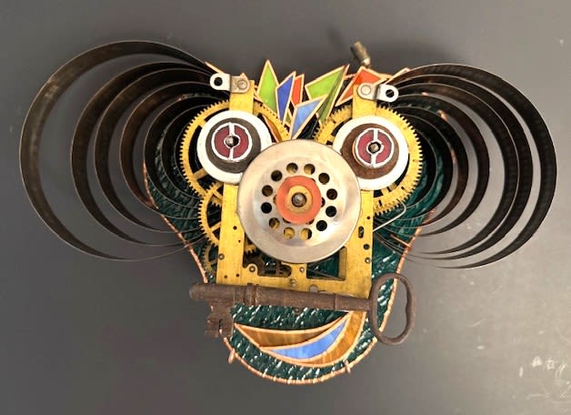 #A022 - "Happy Man" Mask - Bright, playful and undeniably quirky, this wall-mounted stained glass makes a bold gift for birthdays, housewarmings, or milestone celebrations. The piece reads as a cheerful wall mask, its mechanical face and sweeping metal springs create the kind of eye-catching focal point that will make the person you're gifting it to feel noticed and delighted.   Handcrafted from upcycled metal parts, the composition pairs textured black and darker metal with pops of yellow, green, red, blue and orange paint for a lively color story. Circular gears and a perforated disc form the eyes and nose, a large antique-style key suggests a smiling mouth, and curved metal springs fan outward like dramatic hair or horns. Painted metal accents and a circular metal base give the sculpture depth and presence on any wall, while the mixed-color palette lets it complement modern, eclectic, or industrial interiors. Perfect for the creative friend, maker, or anyone who prefers artful, unconventional décor, this piece arrives ready to hang and instantly transforms a room into a conversation-starting space.   Shipping available - select Delivery, then message us to ship.