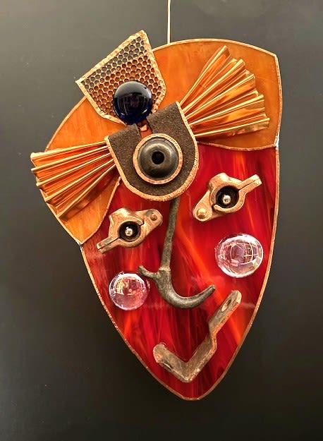 #A034 - "Elegant Lady" Mask - A striking red-and-orange stained glass wall mask that reads like a modern, sculptural portrait-perfect as a distinctive gift or striking accent for anniversary, housewarming, or gallery-style home décor. The stylized face and whimsical headdress create an immediate visual impact; the person you're thinking of will see it as a bold, artful statement that livens a hallway, study, or living room. Crafted from deep red marbled glass with bright orange panels and copper-toned edging, the piece uses mixed-media metal hardware to form expressive eyes, nose, and mouth for an industrial yet playful character. Clear glass orbs and beads are inset along the lower portion to catch light and add reflective texture, while a fan-like metal detail and textured top panel suggest hair or a headpiece. Measures 10.5" H x 7" W x 1" D and arrives ready to hang with included metal hardware.   This is the kind of unique home décor that marks a memorable occasion-housewarming, birthday, or a thoughtful "just because" gift for someone who loves handmade, artsy accents. Special orders are welcome; if you'd like a variation in color or hardware, we can discuss custom options.  Shipping available - select Delivery, then message us to ship. 