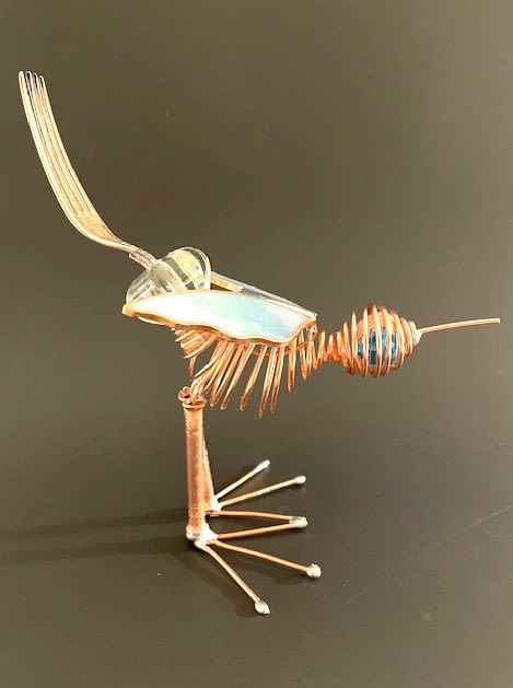#A063 - Bluebird - A whimsical copper-wire bird sculpture that doubles as a delightful decorative accent-perfect as a small gift for a birthday, housewarming, or to mark a personal milestone. This bird figurine uses coiled copper wire for a rounded, spiral body and slender copper rods for its single upright leg and splayed toes, giving it a lively, sculptural silhouette that will make the recipient smile and spark conversation. Delicate iridescent/stained-glass-style wings, and an antique cabinet door pull add shimmer and light, while a blue glass bead near the head provides a bright focal point against warm metallic tones. A repurposed metal fork rises from the back as an unexpected crest or tail element, emphasizing the piece's upcycled, handmade charm; the figure rests on a textured stone base for stable display. Sized for desks, shelves, windowsills, or mantel corners, this compact, playful sculpture is an artful way to say "I'm thinking of you" to someone who appreciates quirky, handcrafted décor.  Shipping available - select Delivery, then message us to ship.