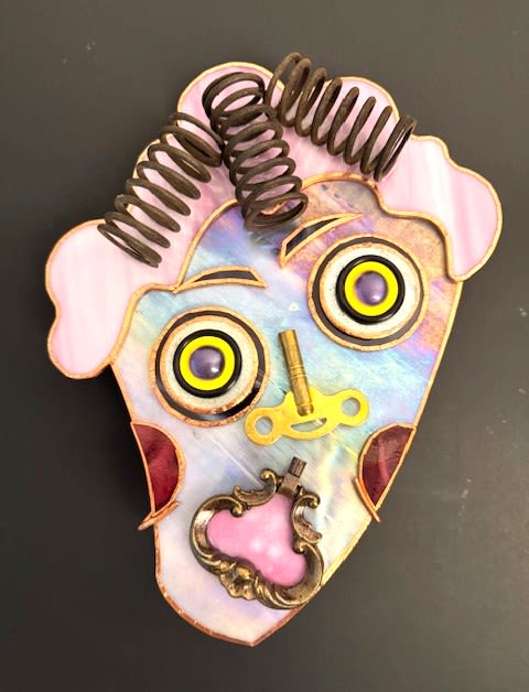 #A069 - "Curlers" Mask - A quirky stained-glass face mask that reads like wearable folk art - this unusual-styled decorative accent blends pastel iridescent glass with bold yellow-and-black eye details for a delightfully surprised expression, as if freaked out about what she looks like with her curlers in. As a gift for birthdays, housewarmings, or just-because moments, this "mask" brings a playful, offbeat charm that will make the person you're thinking of smile and spark conversation in a creative home or office.   Handcrafted from iridescent pastel panels and soft pink glass at the hairline and chin, the piece uses coiled metal springs for curled hair and layered metal hardware-including a small golden key, ornate frame piece, screws, and circular elements-to create facial features with texture and depth. The contrast of shiny glass and aged metal gives a steampunk-upcycled vibe; colors include pink, mixed iridescent tones, yellow, red accents, and black. Sized as a small decorative ornament, it arrives ready to display as a tabletop accent or hung where its light-catching glass and whimsical expression can be enjoyed.  Shipping available - select Delivery, then message us to ship.