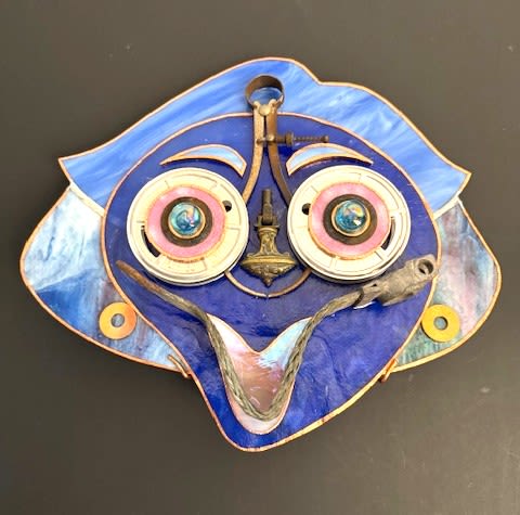 #A107 - "Helpful Lady" Mask - A bright, playful face in vivid blue tones greets the room-this mixed-media wall plaque is a steampunk-style gift for someone who loves artful decor and whimsical accents. As a decorative piece for a birthday, housewarming, or to say "thank you," the stylized face reads as joyful and personal; the person you're thinking of will feel noticed and amused by its quirky, animated expression.   Handcrafted from marbled and blue stained glass with copper edging, the piece combines layered metal hardware, brass elements, and round mechanical components to add texture and depth. Two large circular eyes are rimmed in white and pink with small iridescent centers that catch the light, while curved metal pieces form expressive eyebrows and a broad smiling mouth. Additional round disc elements and an electrical cable woven into the composition give it an industrial-art vibe that works in modern or eclectic interiors. Perfect for a creative studio, living room wall, or gallery-style display, this plaque is the kind of unconventional gift that sparks conversation and brings a cheerful energy to any space. It's a thoughtful way to celebrate birthdays, house warmings, or to simply brighten someone's day-order with confidence for immediate wall-ready decor that requires only a secure hook or nail for hanging.  Shipping available - select Delivery, then message us to ship.