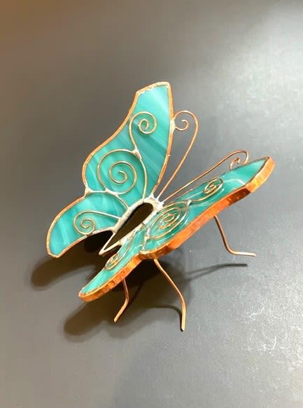 #A111  Turquoise Resting Butterfly - A whimsical pop of color, this small gift for display on a tabletop is a turquoise stained-glass resting butterfly keepsake, perfect for a birthday bouquet or a "thinking of you" surprise. The resting butterfly, with teal glass wings edged in warm copper wire spirals, catches light and adds an artistic touch that immediately draws the eye and feels delightfully personal for the person you're celebrating. The sculpture is created with lively contrast and visual movement around the metal wire frame that supports the butterfly.   Textures are layered-glossy stained glass and warm copper edging, reminding the recipient of spring and summer, both in color and tactile appeal. Sized as a small tabletop piece, it works equally well on a bedside table, desk, or mantel and arrives ready to. Choose this as a keepsake-accompanied bouquet for someone who appreciates handmade, artistic touches. Care is simple: display the stained-glass figurine indoors as a lasting reminder of your thoughtfulness.  Shipping available - select Delivery, then message us to ship.
