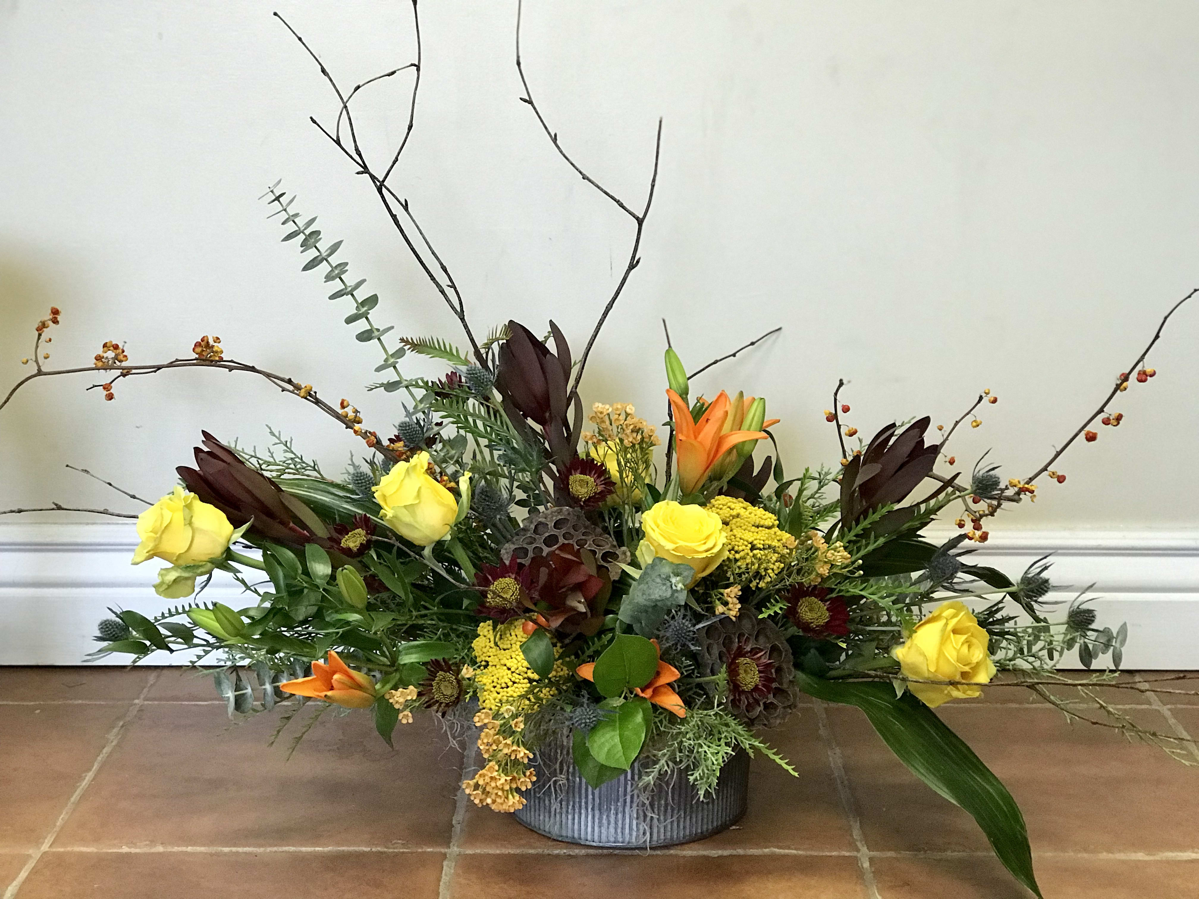 Low floral arrangement with yellow roses and orange lilies in a gray container