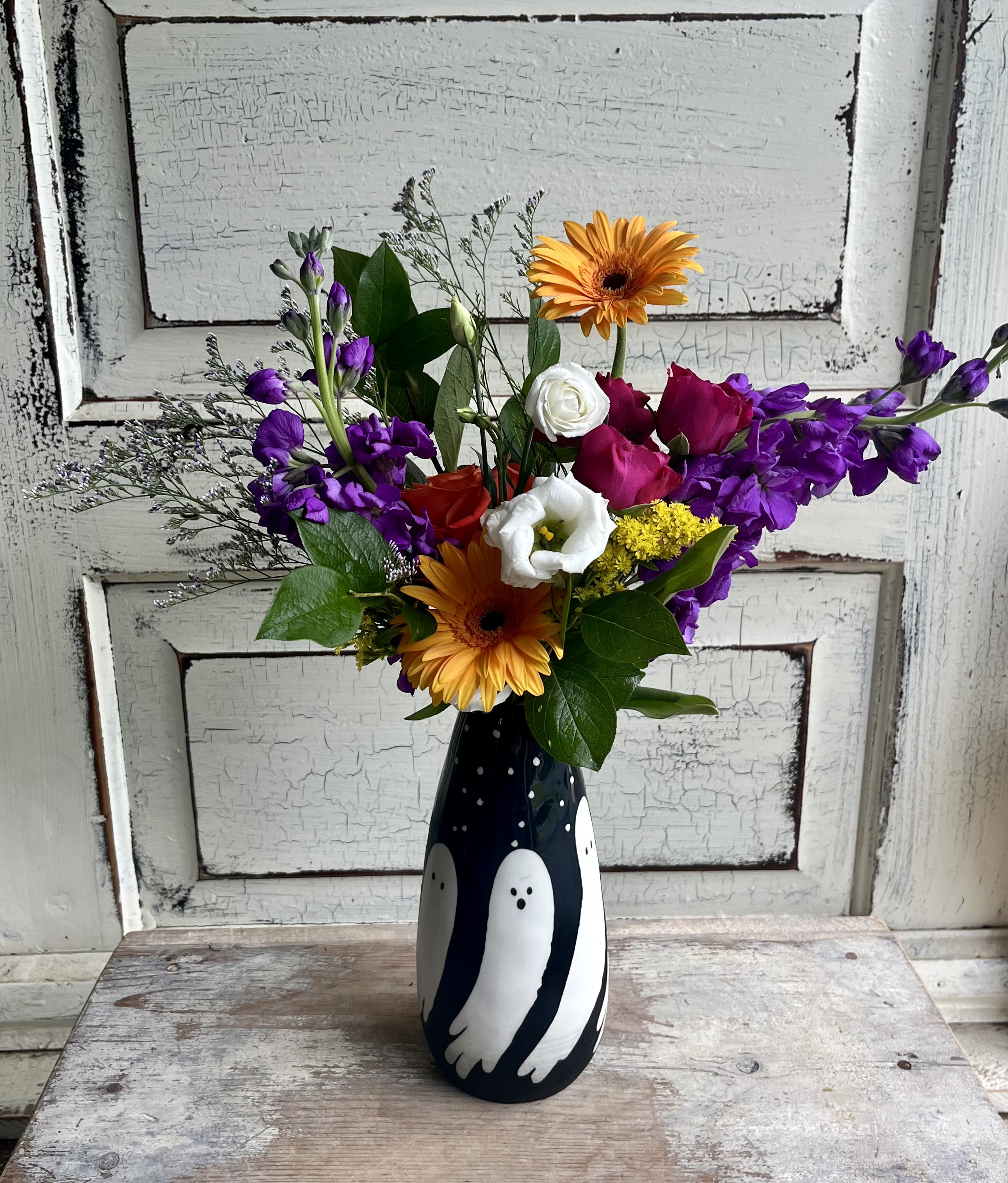 Mixed bouquet with orange gerberas, purple flowers, and roses in a black vase