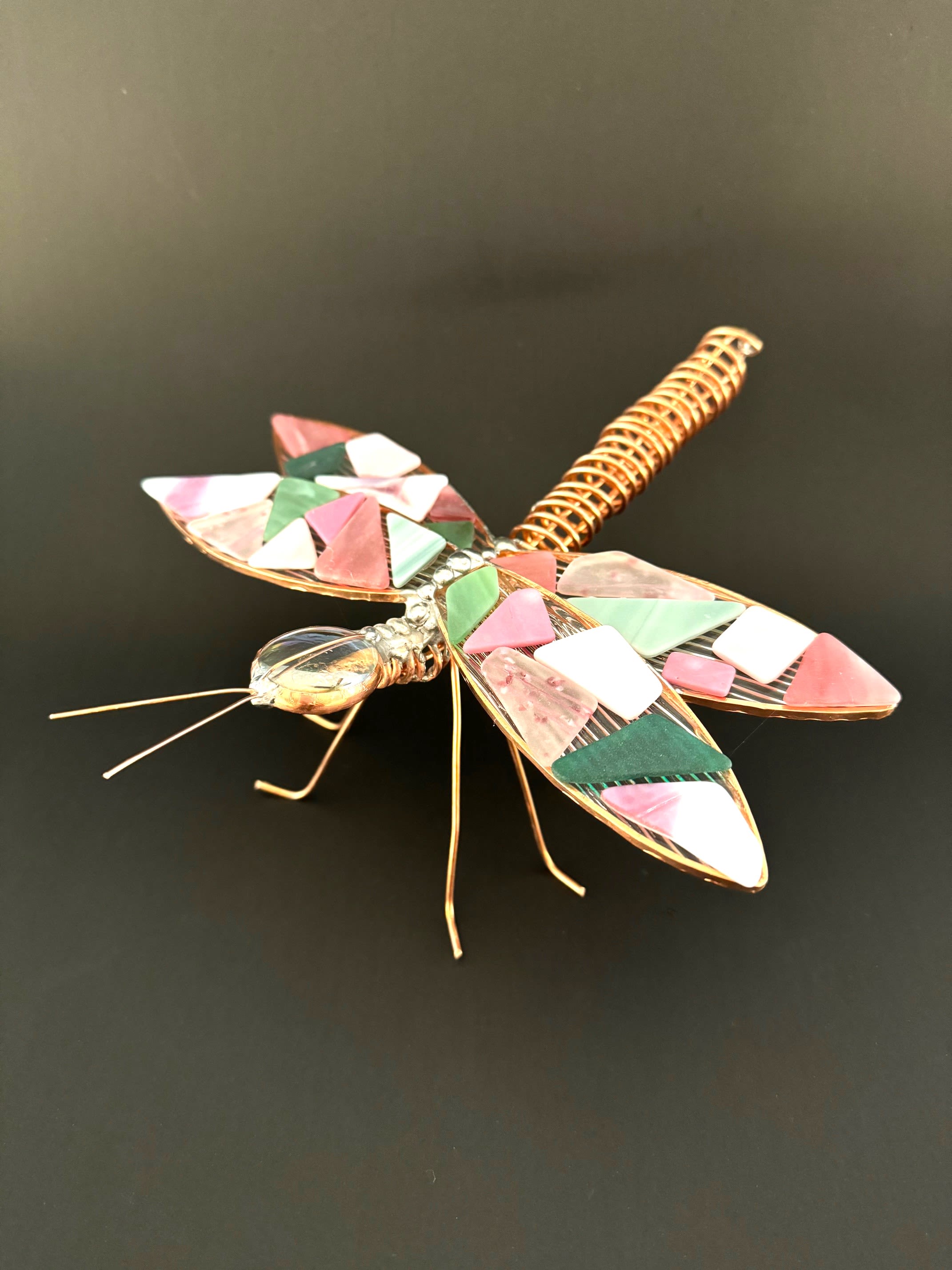 #A116 - "Earth" Mosaic Dragonfly - A playful, handcrafted dragonfly accent that brings warm, autumnal color to any tabletop or bouquet - perfect as a seasonal gift accent or a whimsical housewarming touch. This decorative metal and mosaic glass sculpture works beautifully as an accent for an anniversary bouquet or as a standalone home décor piece to celebrate someone who loves nature and crafty details.   The piece features a coiled, copper-toned metal body with fine wire legs and antennae for a delicate, handmade profile. Its wings and are covered with small mosaic glass tiles in shades of orange, yellow, red, pink and maroon, creating a jewel like effect that glows against darker backgrounds. The contrast of shiny metal and matte mosaic gives it an artistic, tactile quality.   Tuck it into a mixed-color arrangement to add sparkle and texture, set it beside a potted plant, or present it on its own as a thoughtful accent that says you notice the little things. Lightweight and easy to place, it's ideal for seasonal décor, hostess gifts, or a charming finishing touch to a gift bouquet.  Shipping available - select Delivery, then message us to ship.