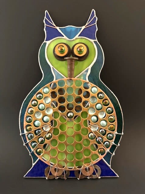 #A130 - Blue &amp; Green Brass Bellied Owl -  A playful metal and glass owl arrangement that doubles as a bright decorative accent for birthdays, housewarmings, or to celebrate a personal milestone. This Brass Bellied- Owl pairs blue and green glass panels and metal hardware - with cheerful yellow and orange highlights to create a modern, whimsical gift the recipient will display long after the day has passed.   The owl's round belly is a mosaic of shiny glass marbles in green, gold, and pastel metallics set into a honeycomb grid, while layered metal eyes and a central beak add character and texture. Wire accents and a scrolling black metal display stand give it gallery-style presence on a mantel, entry table, or office shelf or hung on the wall. Sized to be a standout tabletop piece, it comes ready to display and makes the person you're thinking of feel seen with a fun, contemporary touch.  Shipping available - select Delivery, then message us to ship.