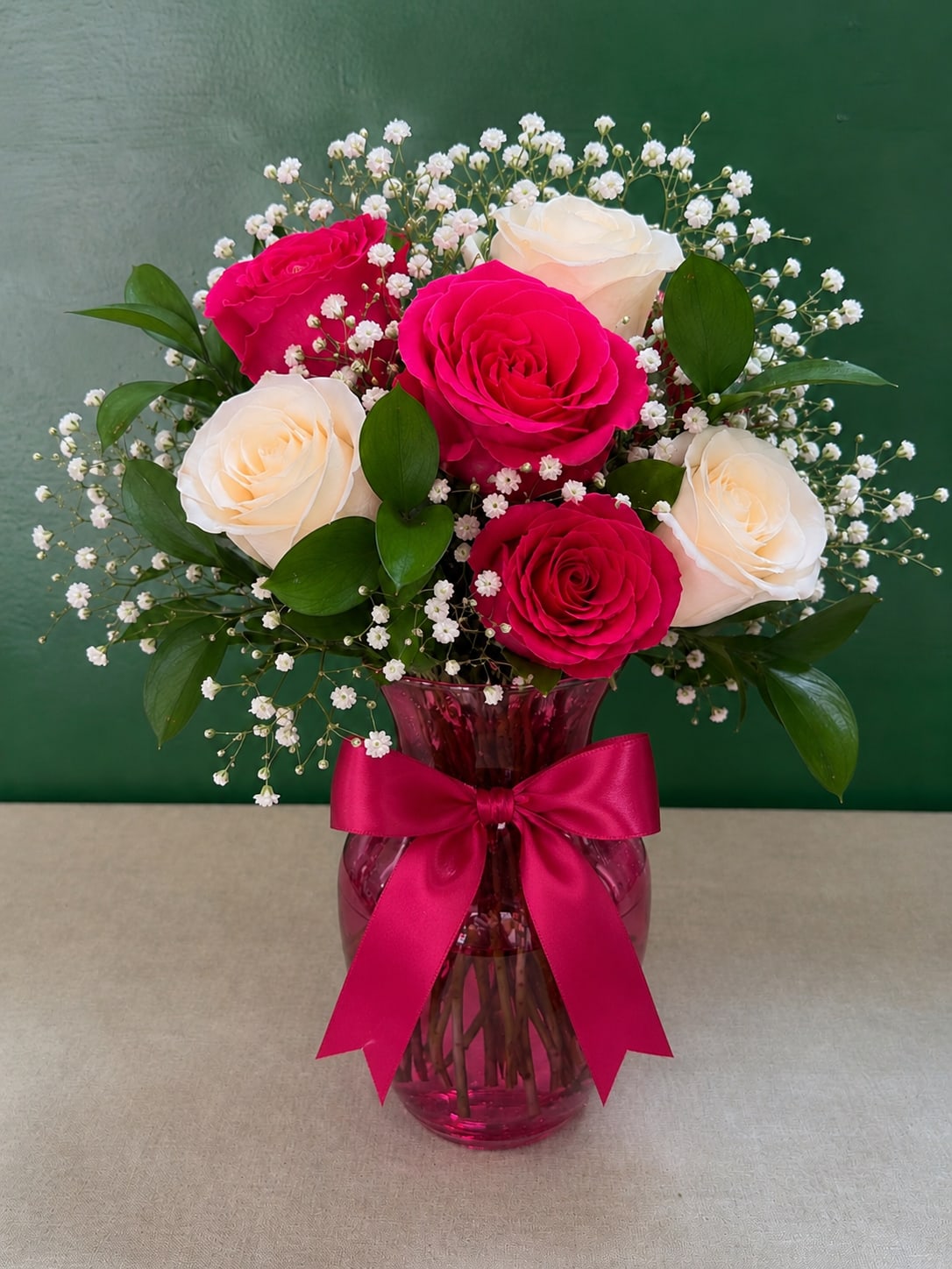 Pink and white roses in a magenta vase with a ribbon bow