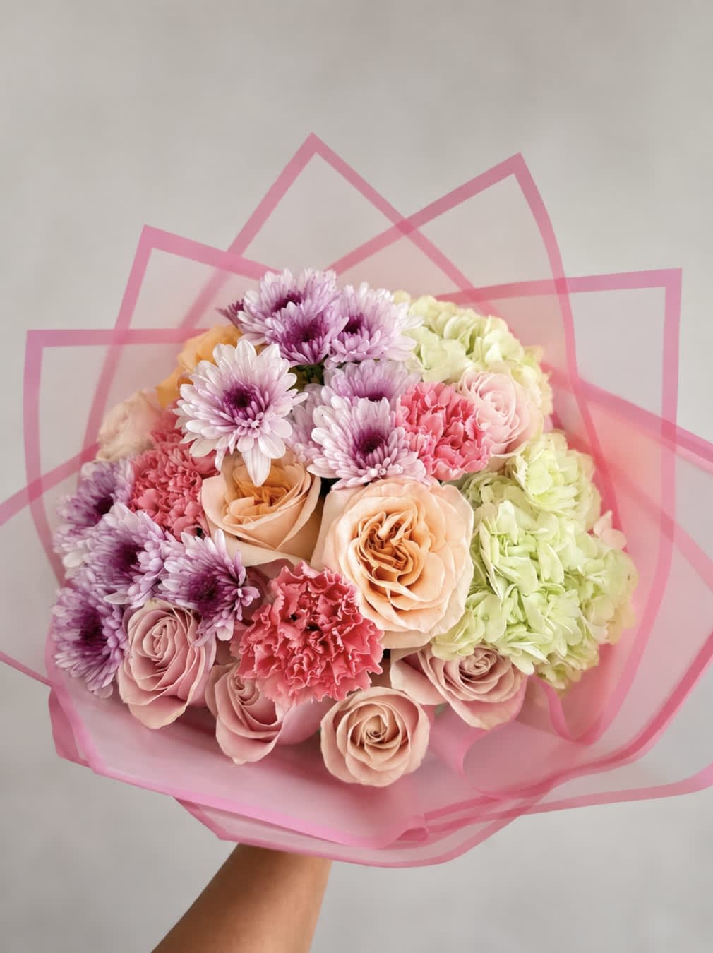 Bouquet of pink and peach roses with purple daisies and hydrangeas in pink wrap