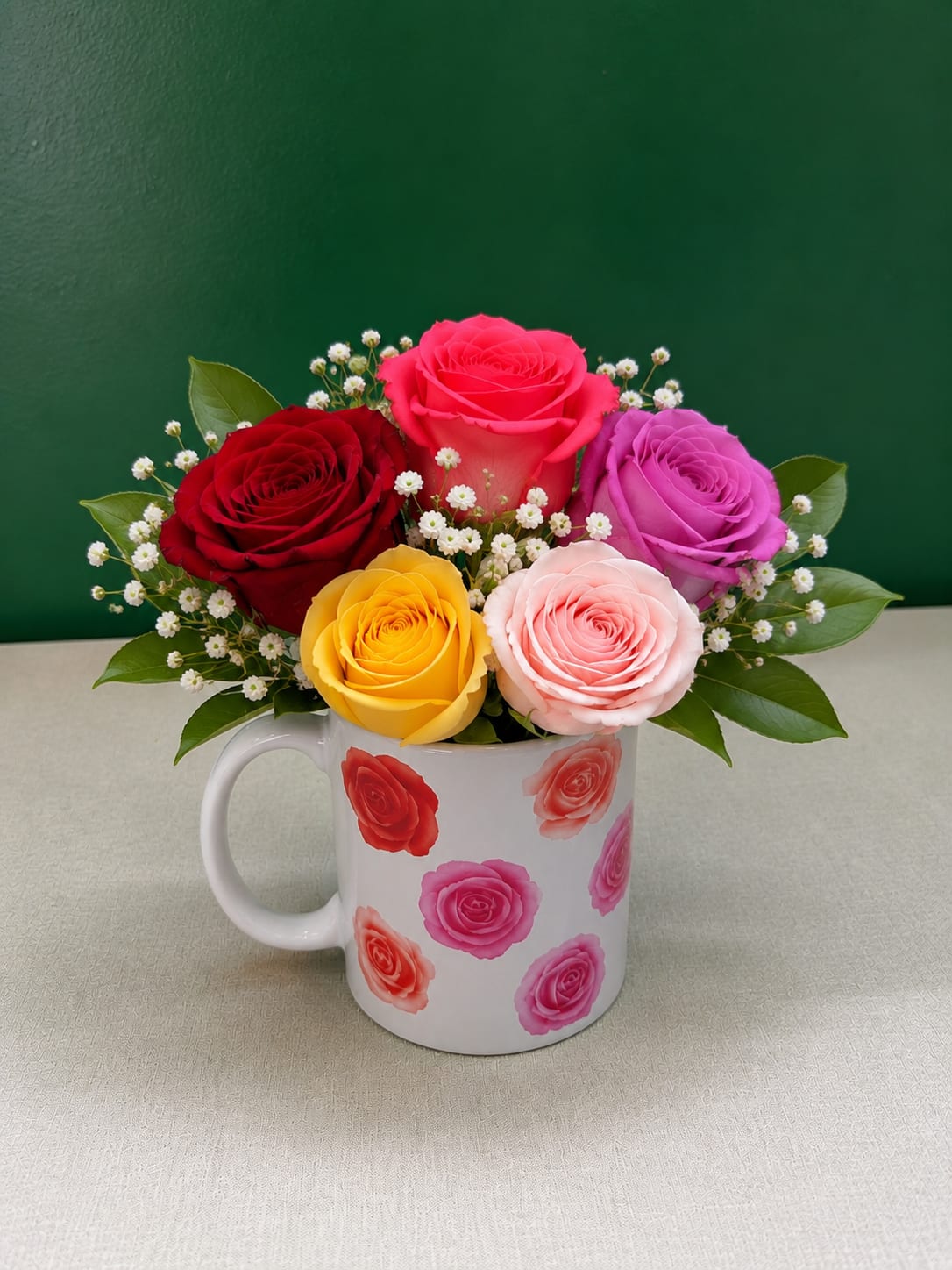Colorful roses arranged in a white mug with small white filler flowers