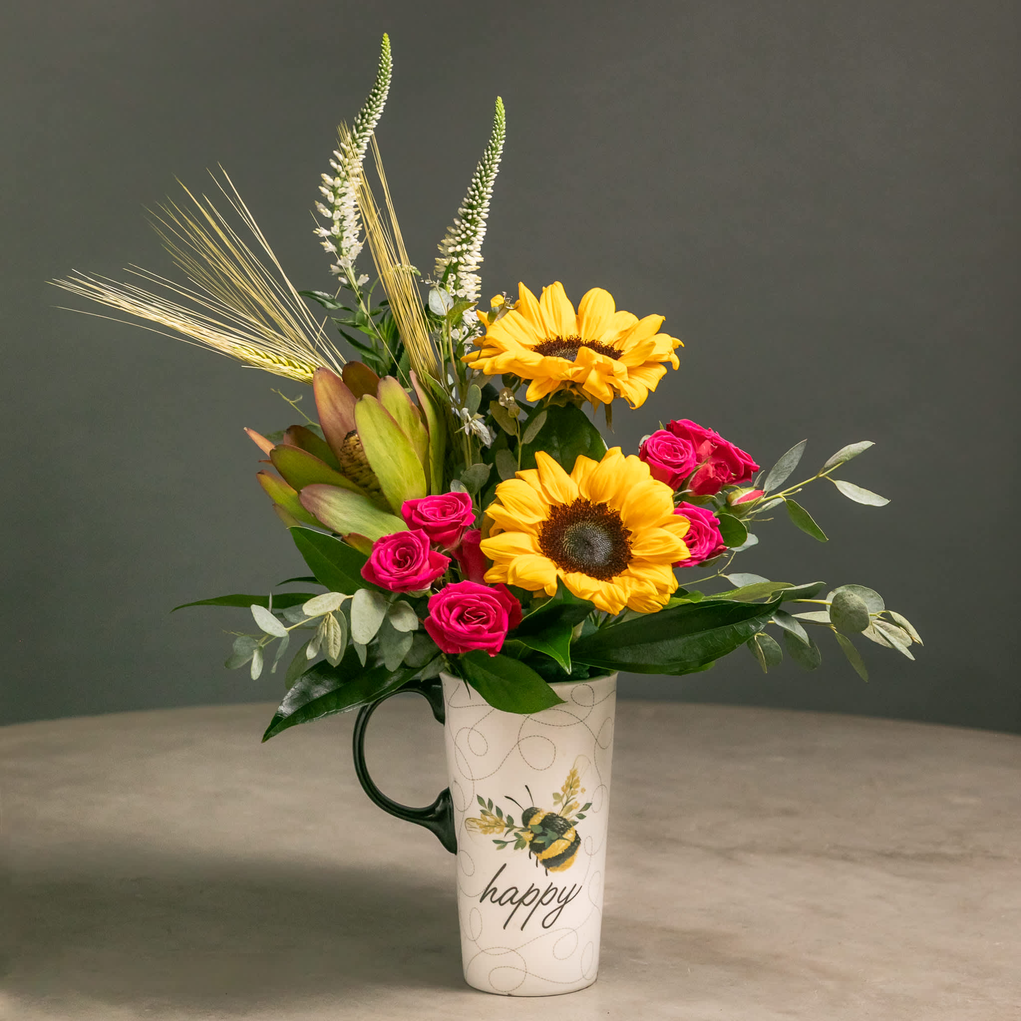 Sunflowers and pink roses arranged in a tall mug with a "happy" design