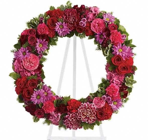 Circular wreath of red, pink, and purple flowers on a white stand