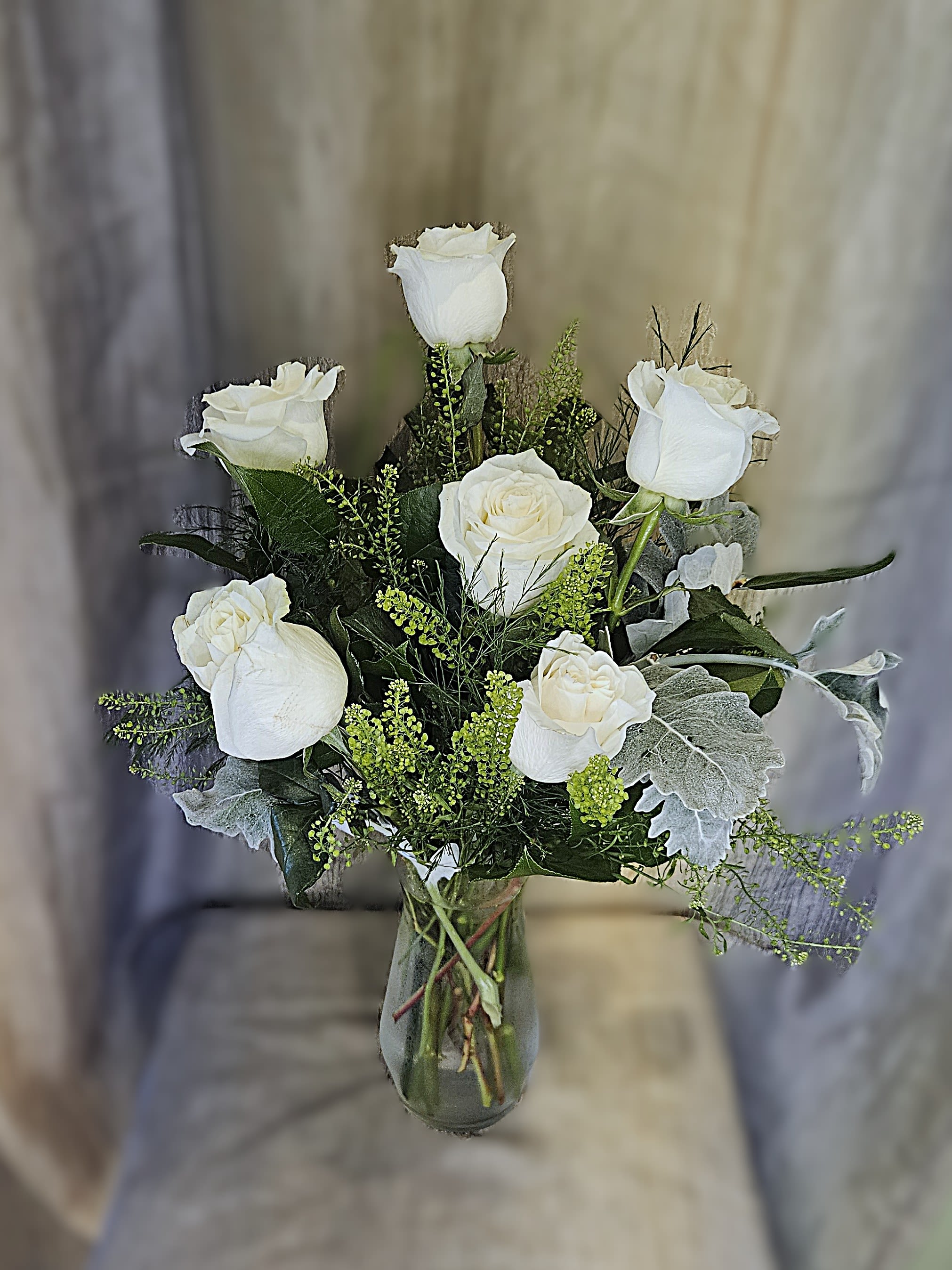 White roses arranged in a glass vase with silvery foliage