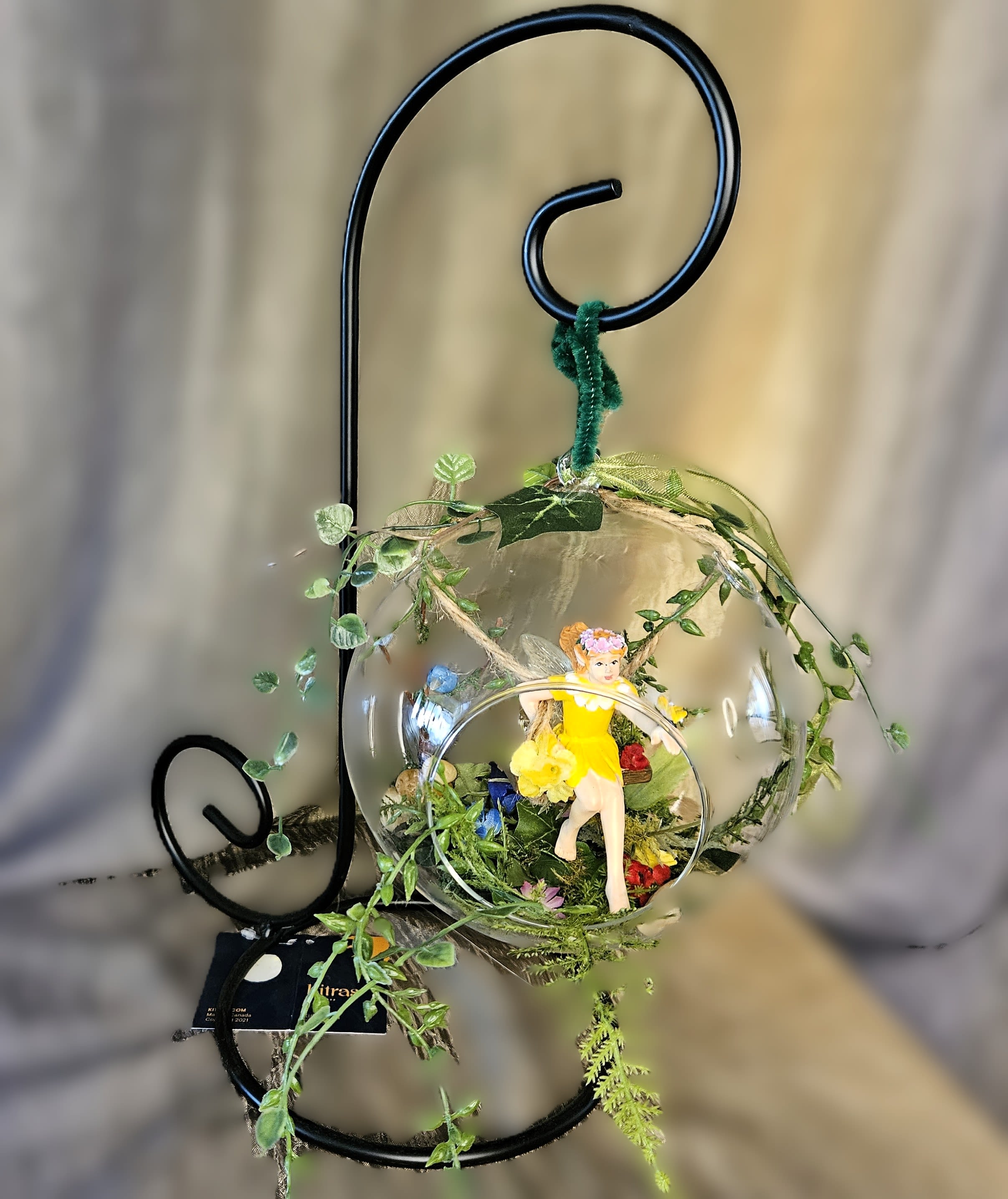 Glass ornament with a small fairy figure and tiny flowers on a black metal stand