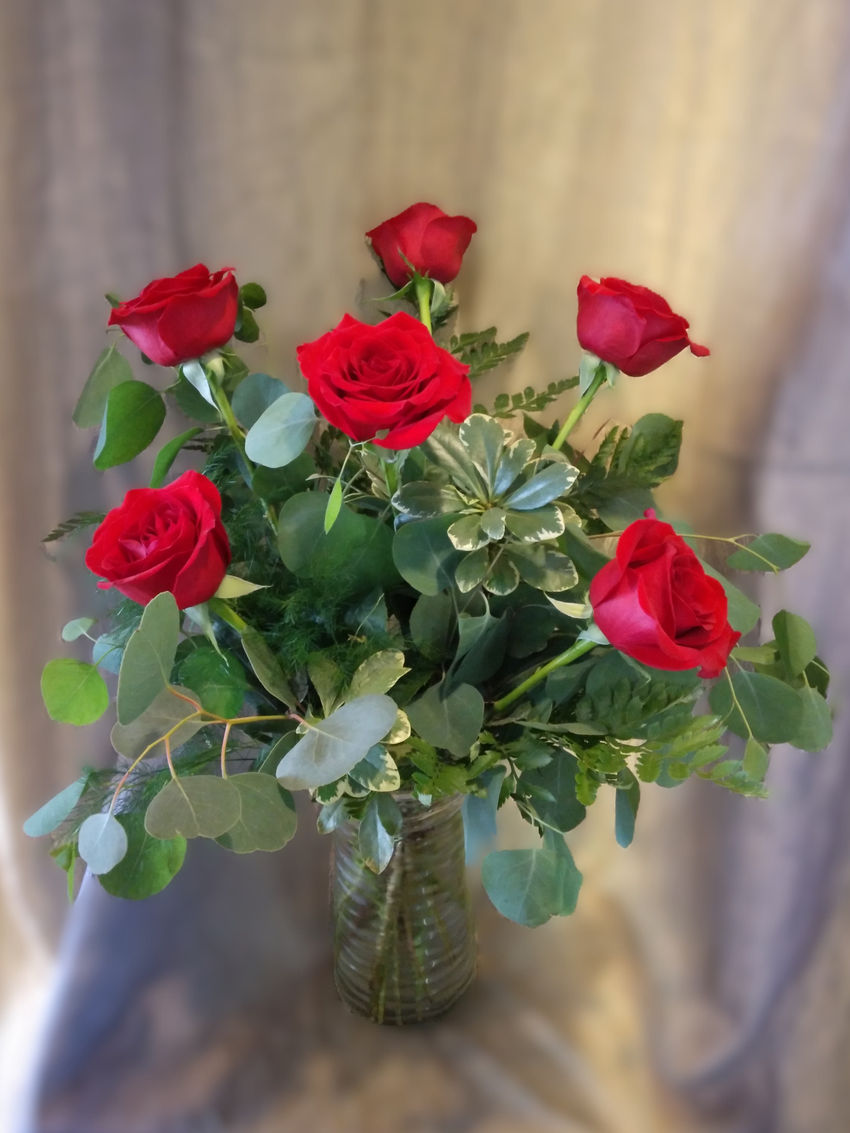 Red roses arranged in a clear glass vase with mixed greenery
