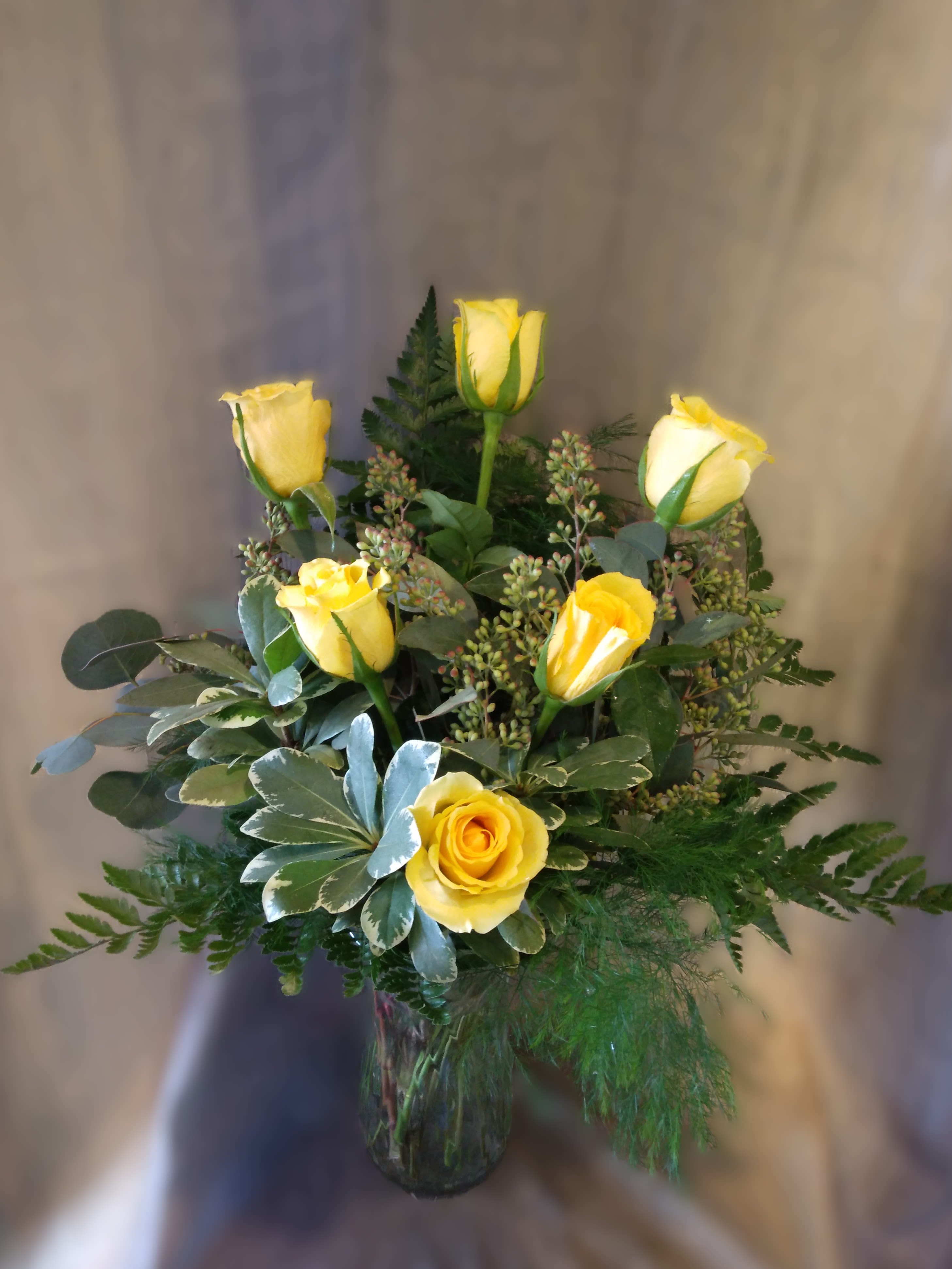 Yellow roses arranged in a glass vase with mixed greenery