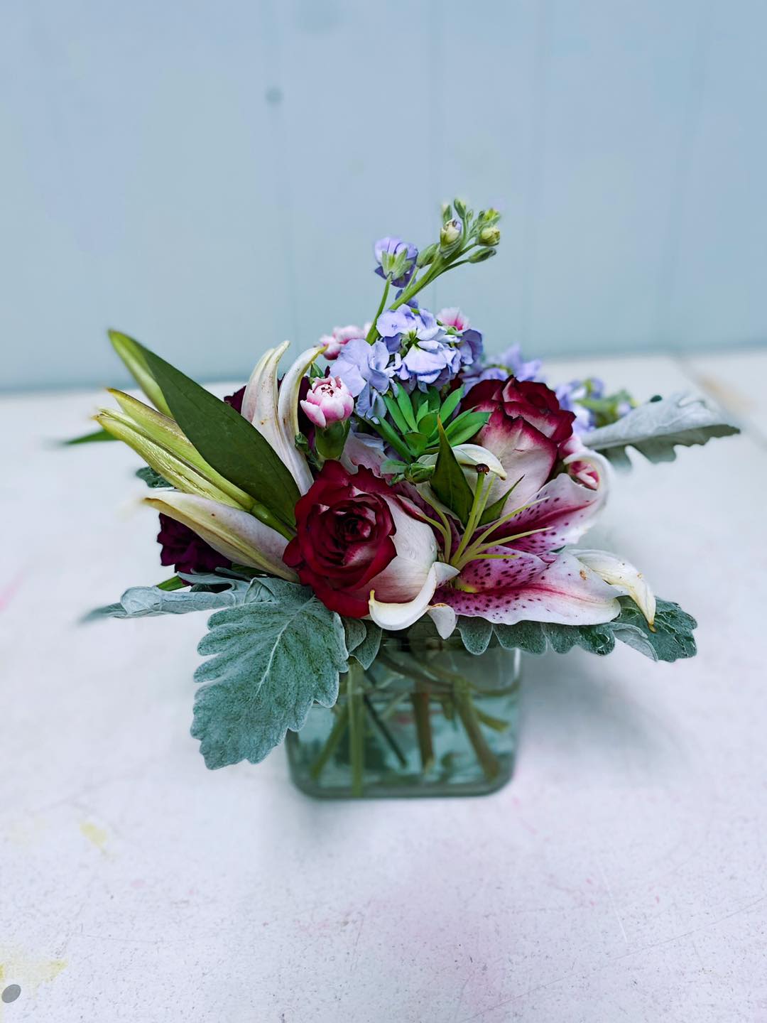 Mixed bouquet in a square glass vase with roses and lilies