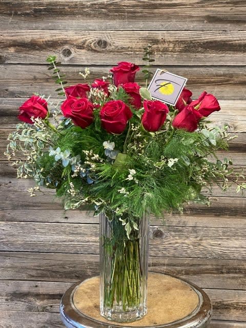 Red roses arranged in a tall glass vase with mixed greenery