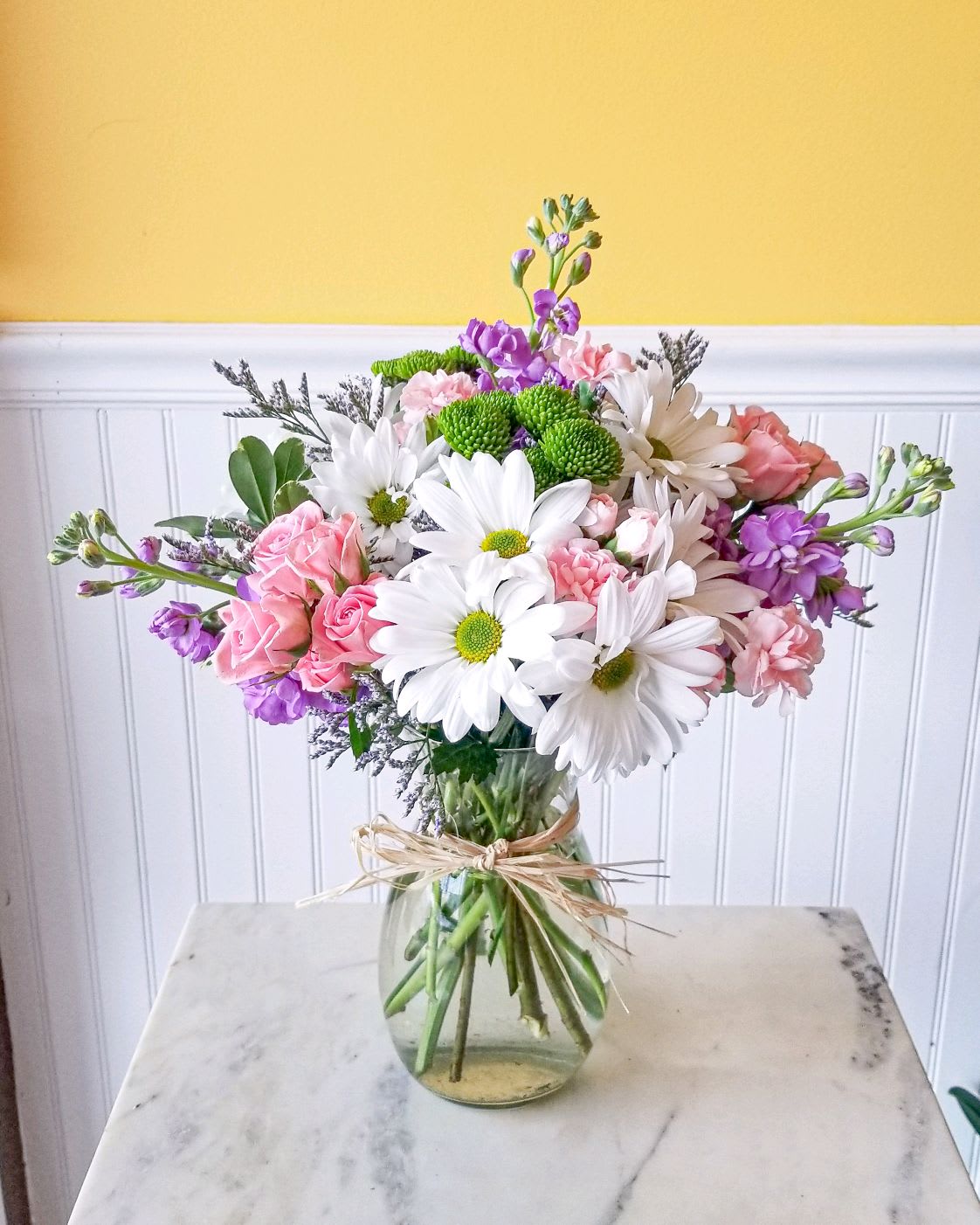 Mixed bouquet of white daisies, pink roses, and purple flowers in a glass vase