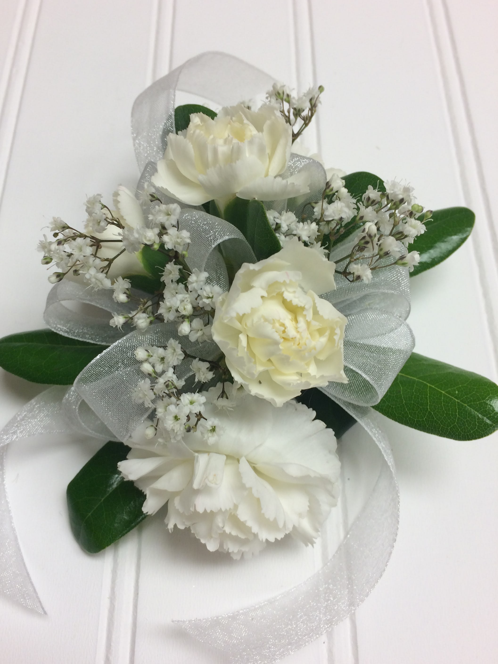 White floral corsage with ribbon and green leaves