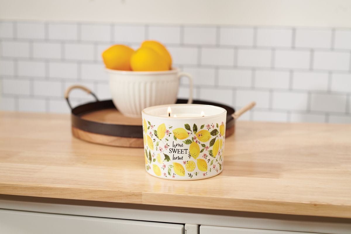 Lemon-patterned candle on a wooden counter with a bowl of lemons behind it