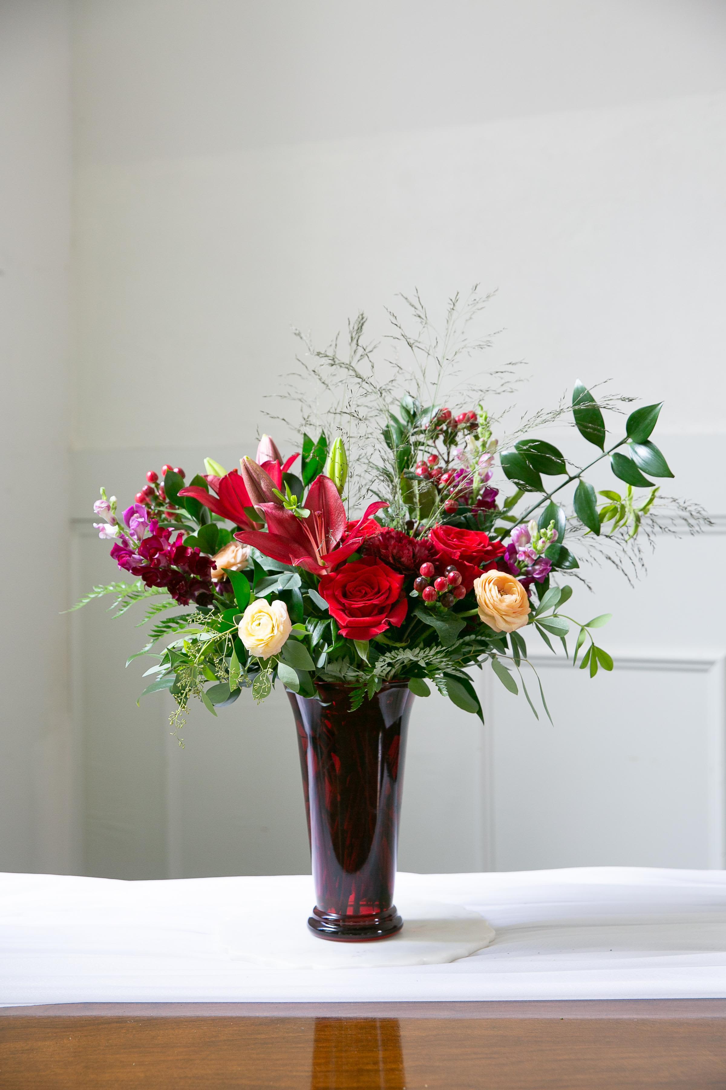 Red roses and lilies arranged in a tall burgundy vase