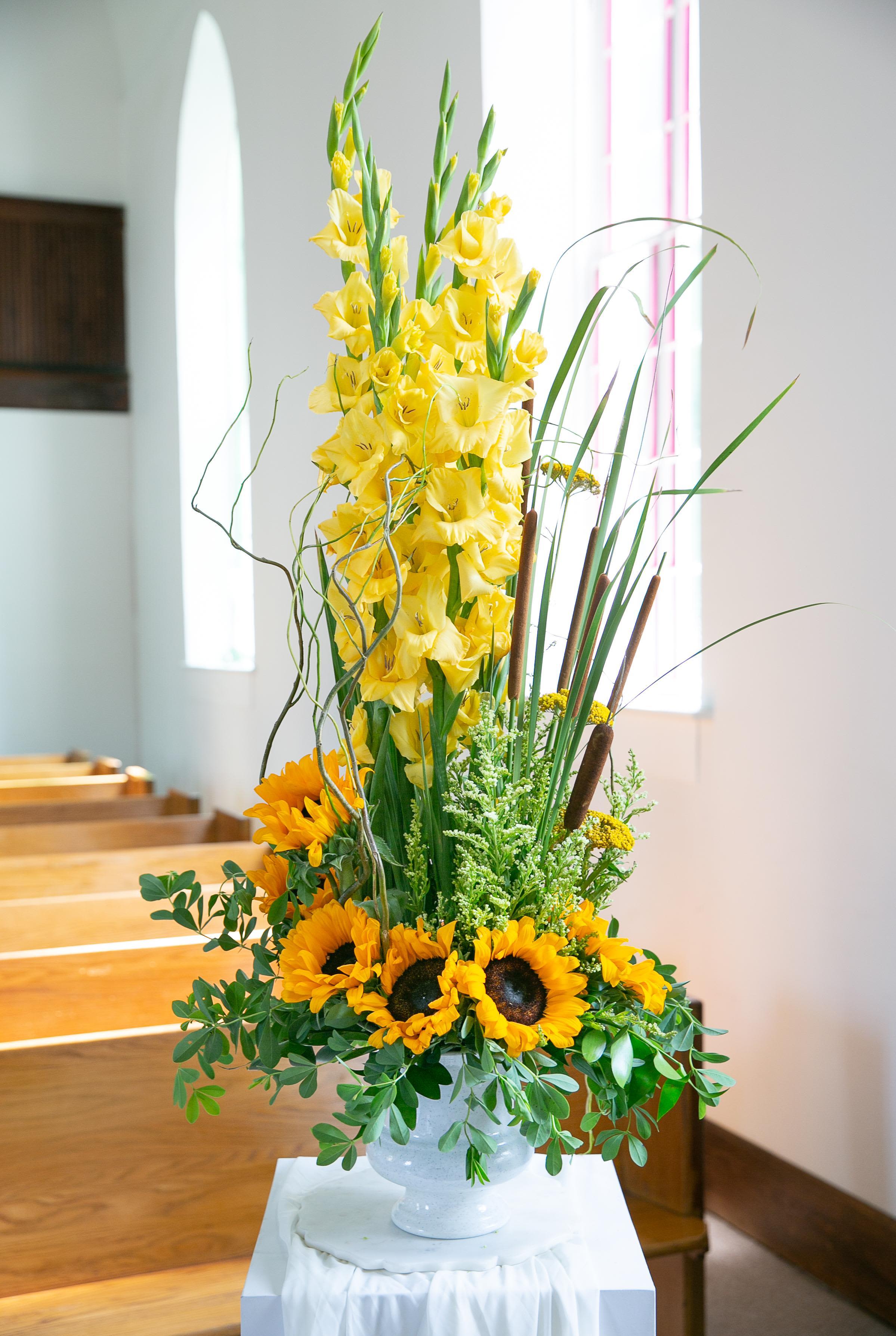 Tall yellow floral arrangement with sunflowers in a white pedestal vase