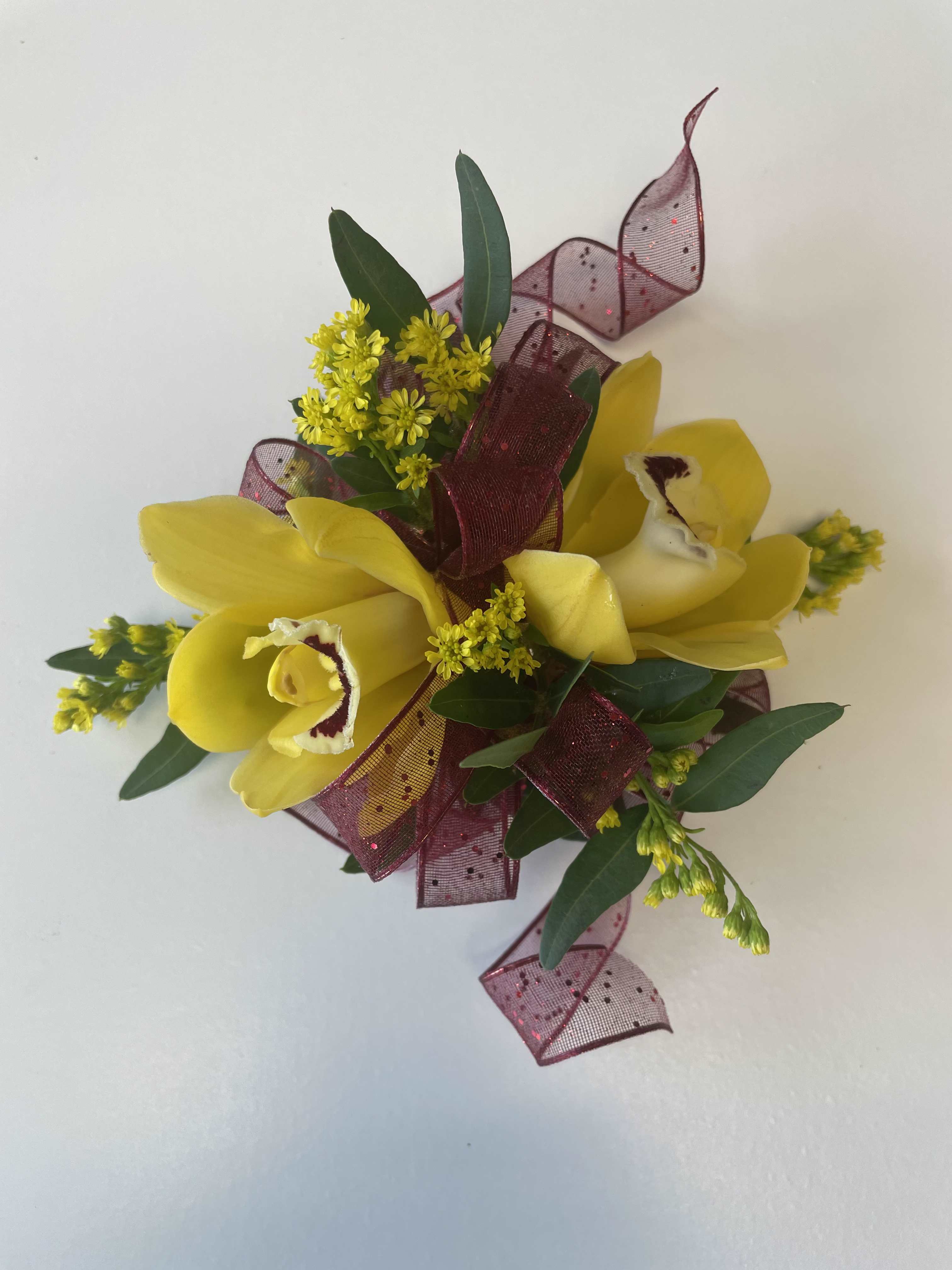 Yellow orchid corsage with burgundy ribbon and greenery