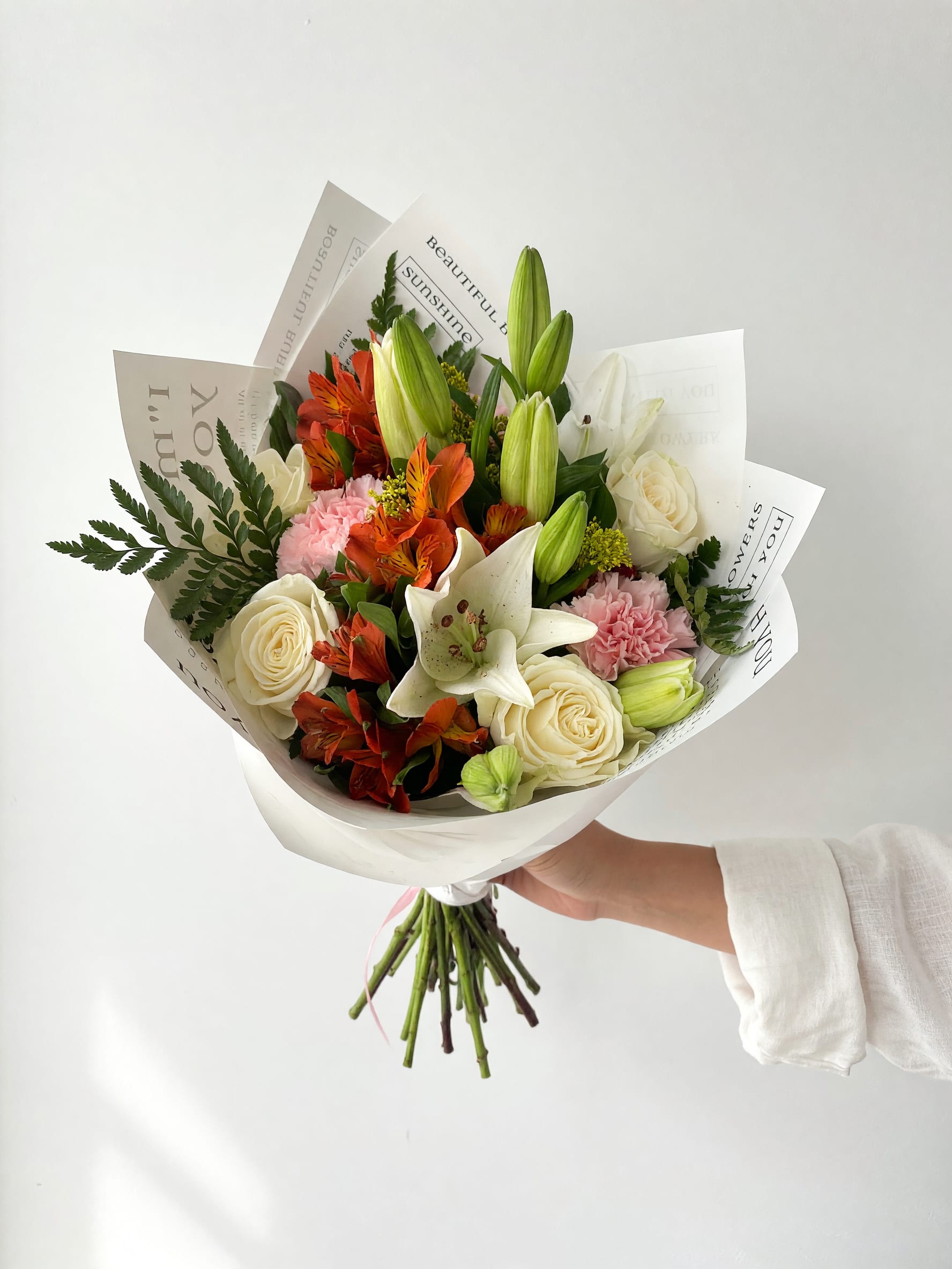 Hand-tied bouquet of white roses, lilies, and orange flowers in white paper