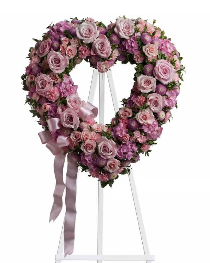 Heart-shaped floral wreath of pink and purple flowers on an easel with ribbon