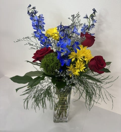 Wings of Peace - A vibrant expression of love, hope, and remembrance, Wings of Peace is a graceful sympathy arrangement designed to offer comfort during times of loss. Featuring striking blue delphinium, classic red roses, and cheerful yellow daisies, this arrangement symbolizes peace, love, strength, and cherished memories. Presented in a keepsake vase inscribed with a heartfelt message: In Loving Memory Those we love don't go away they walk beside us every day unseen, unheard, but always near, still loved, still missing and very dear. It serves as a lasting tribute to those who remain forever in our hearts. Thoughtfully arranged in bright, uplifting colors, Wings of Peace offers a comforting reminder that love endures, memories live on, and the spirit of those we hold dear continues to bring light and peace to our lives. 