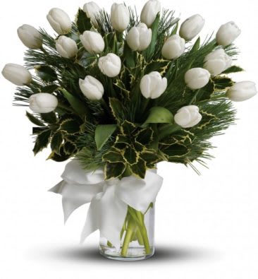 Arrangement of white tulips with pine and holly in a glass vase with a white bow