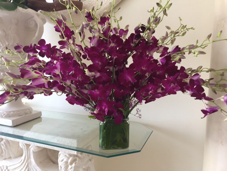 Spray of bright purple dendrobium orchids arranged in a low square glass vase.