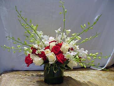 Red and white rose arrangement with white orchids and green sprays in a glass cylinder vase