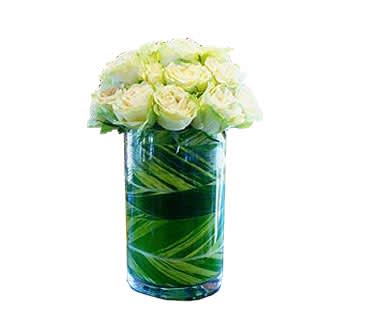 Cluster of white roses arranged in a tall glass cylinder vase lined with green leaves.