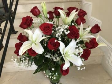 Tall arrangement of red roses and white lilies in a clear glass vase