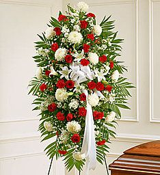 Tall standing spray of red and white flowers with a white ribbon on an easel