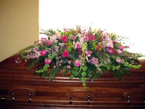 Pink and green casket spray arranged on a polished wooden casket