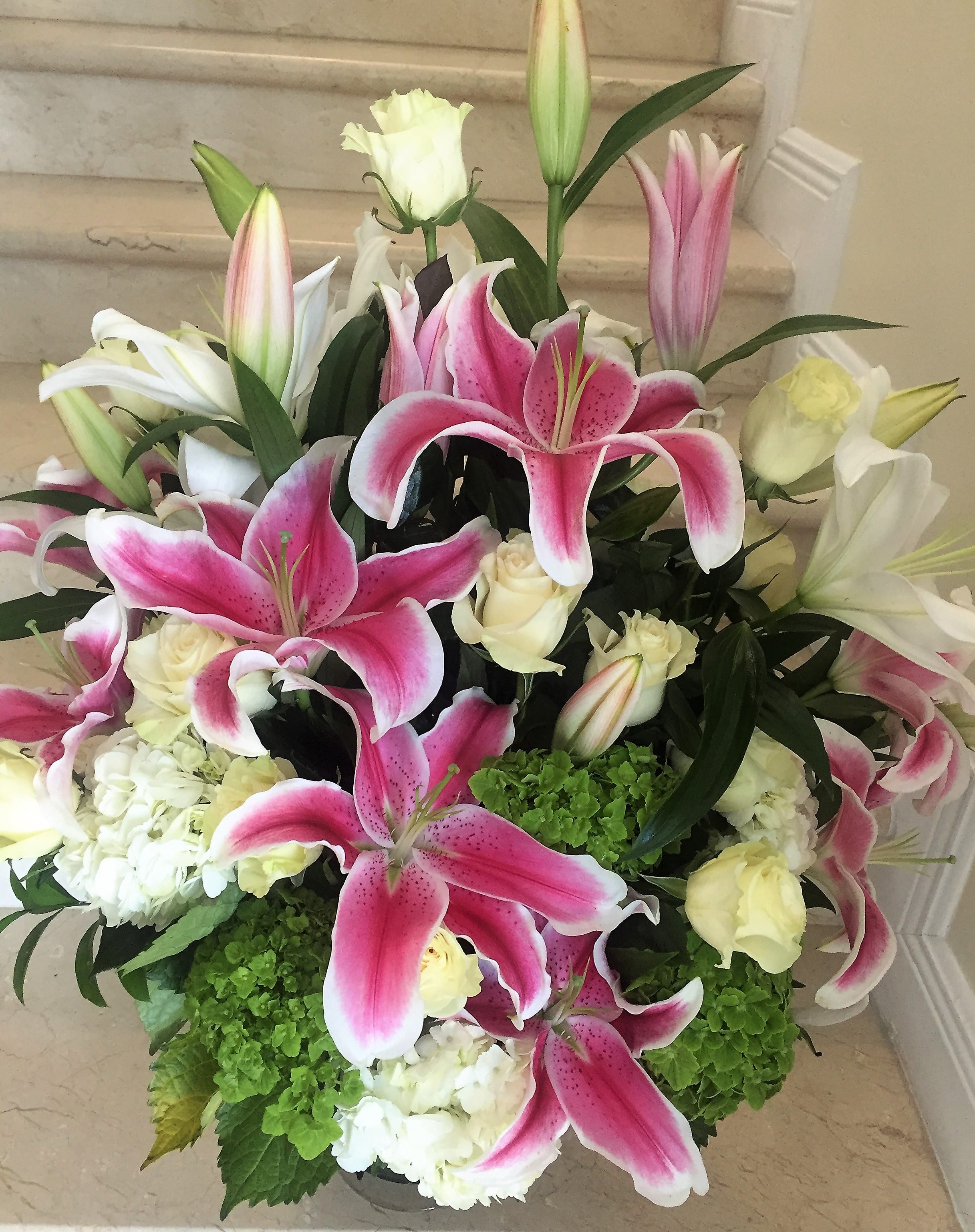Large arrangement of pink lilies, white roses, and hydrangeas in a low container