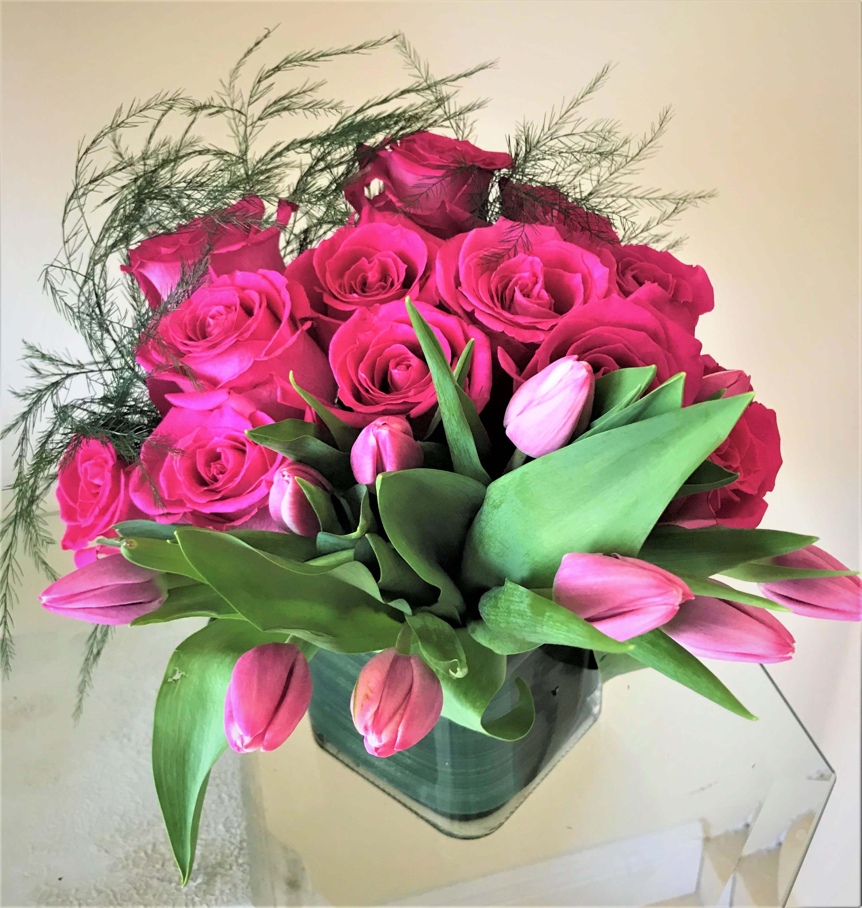Compact arrangement of hot pink roses and tulips in a square glass vase