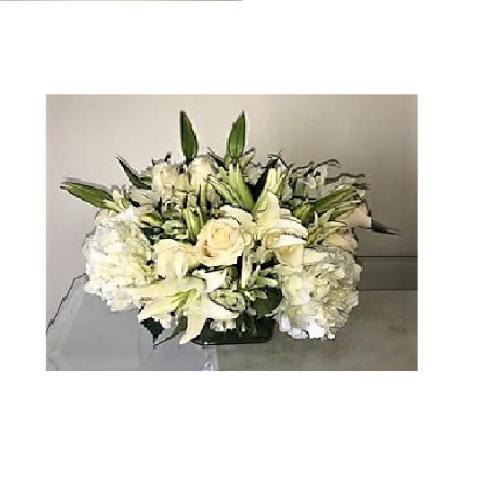 Low white arrangement of roses, lilies, and hydrangeas in a rectangular glass vase