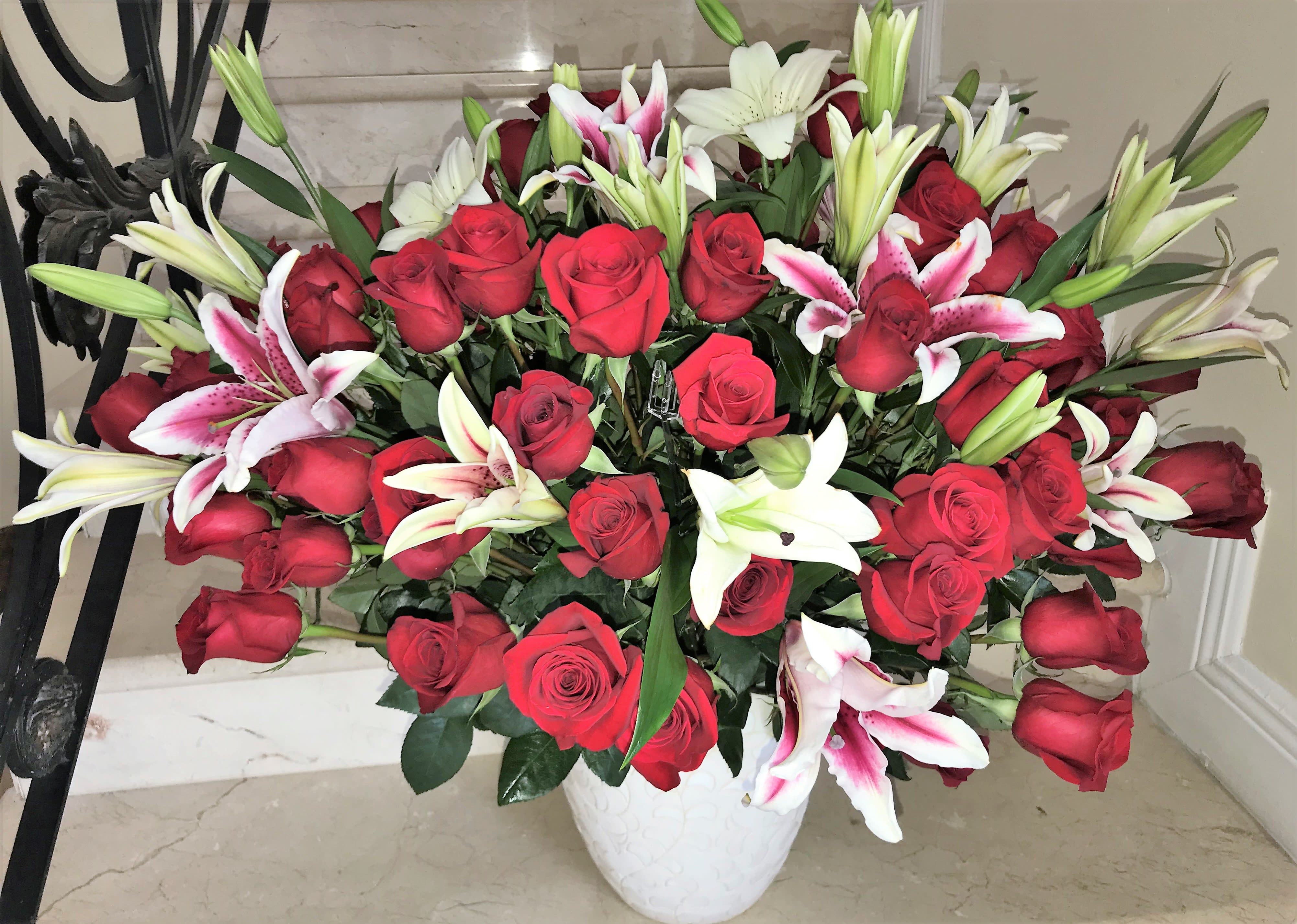 Large arrangement of red roses with white and pink lilies in a white ceramic vase