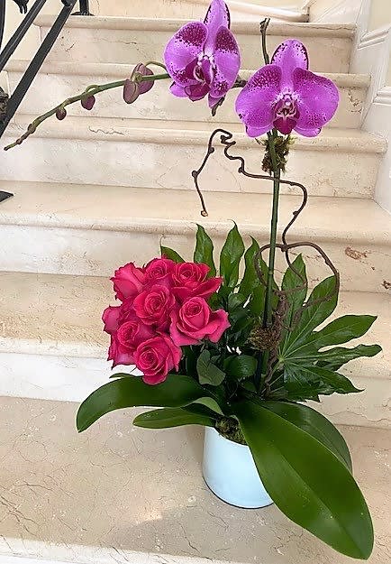 Tall orchid and hot pink rose arrangement in a white pot with lush foliage
