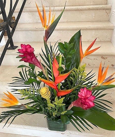 Tall tropical arrangement with orange and pink flowers and lush foliage in a low rectangular container