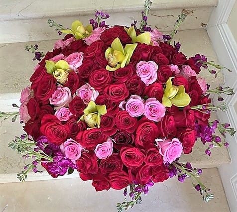 Dense round arrangement of red and pink roses accented with yellow orchids and small purple flowers
