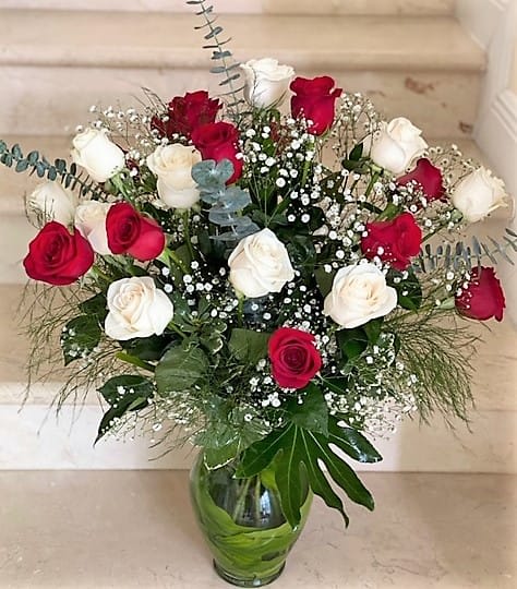 Tall arrangement of red and white roses with baby's breath in a clear glass vase