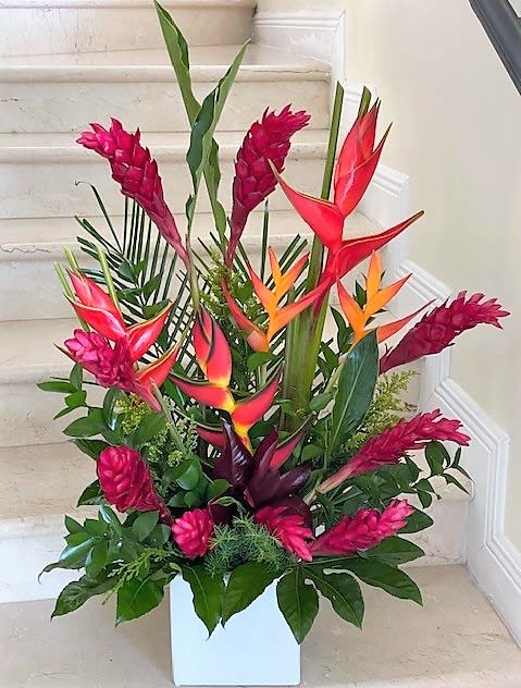 Tall tropical arrangement with red and orange flowers in a white square vase