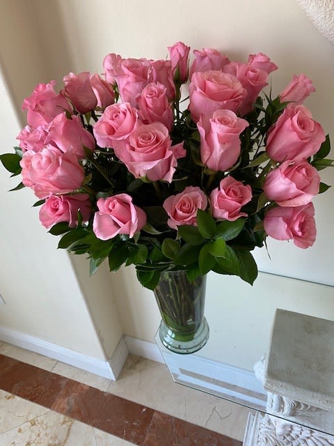 Tall arrangement of pink roses in a clear glass vase on a glass table