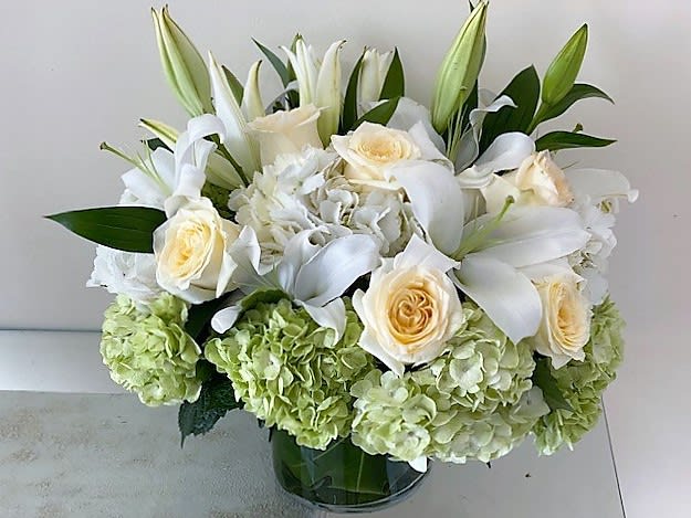 Green and White Elegance - An elegant round arrangement with Green Hydrangeas, White Hydrangeas, White Roses and White Lilies arranged in a glass cube. Beautiful from every corner. Deluxe with more flowers. Premium with much more flowers and a bigger glass vase.